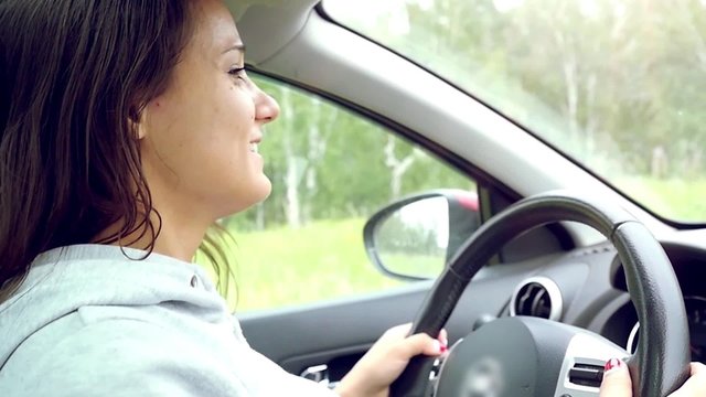 Young beautiful woman drives a car singing, dancing, smiling