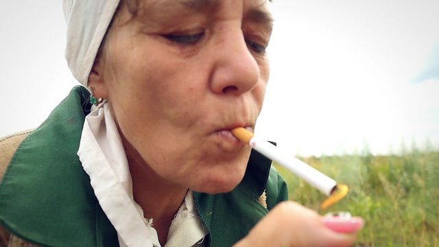 aged woman smoking a cigarette in a scarf on the nature and
