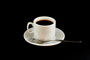 cup of coffee on a saucer with a spoon on a black background
