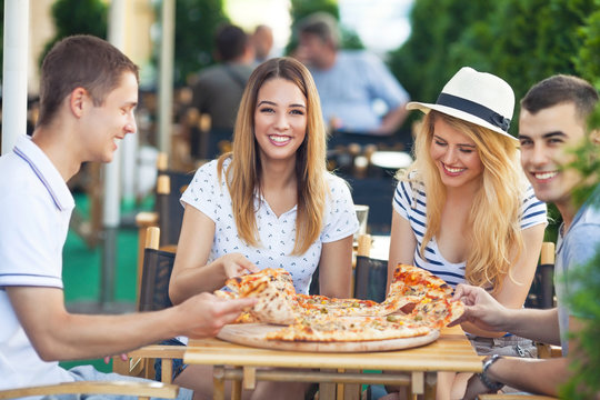 Group of cheerful teenage friends sharing pizza in a outdoor cafe