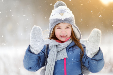 Funny little girl having fun in beautiful winter park during snowfall