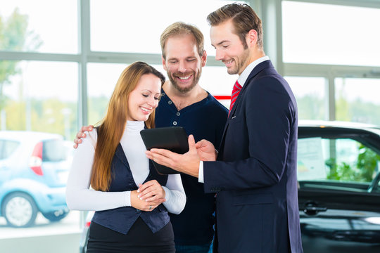 Verkäufer und Kunden mit Auto im Autohaus