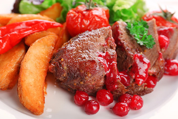 Tasty roasted meat with cranberry sauce and roasted vegetables on plate, on color wooden background