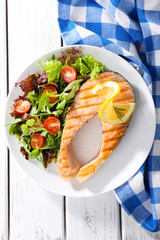Tasty grilled salmon with salad on table close up