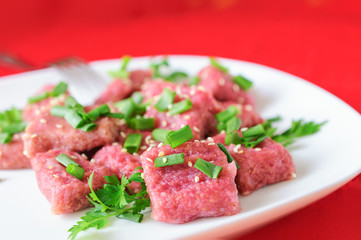 Gnocchi from beet with green onions and parsley on a white plate.