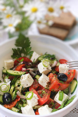 Greek salad on a white plate with a bouquet from camomiles on background.