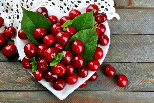 Sweet cherries with green leaves on plate, on wooden background