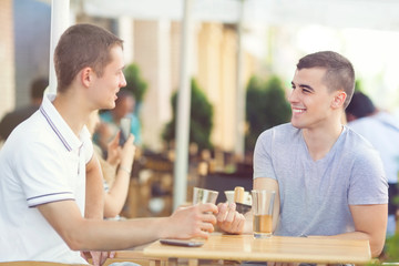 Two young men relaxing in a cafe and drinking beer