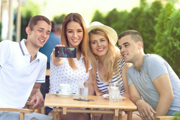 Group of teenage friends having fun in the outdoor cafe taking selfies