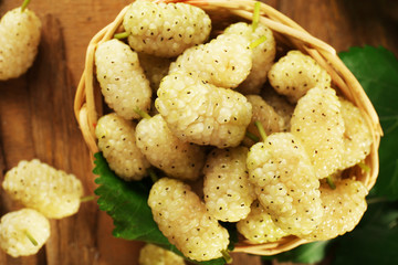 Fresh mulberry in wicker basket on wooden table, closeup