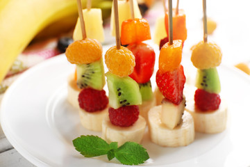 Fresh fruits on skewers in plate on table, closeup