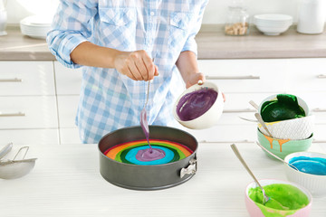 Young woman making rainbow cake in kitchen