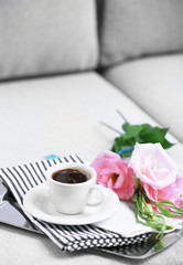 Cup of coffee with flowers on tray on sofa in room