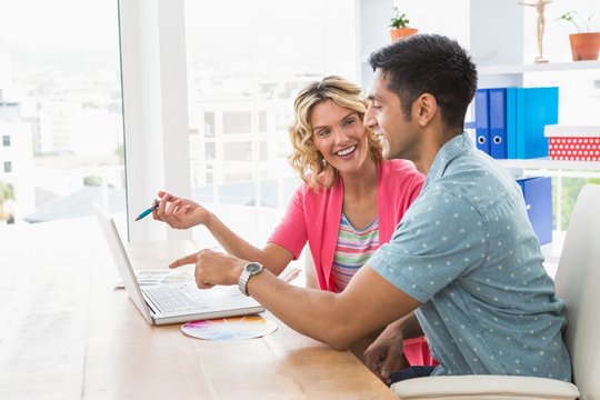 Smiling colleagues working together with laptop 