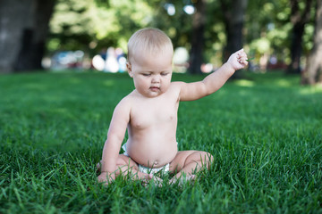 Happy baby with light and fluffy hair sitting on the grass