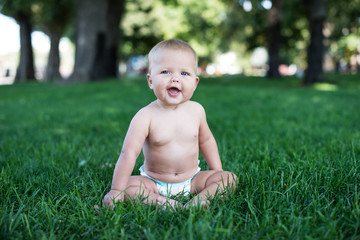 Happy baby with light and fluffy hair sitting on the grass