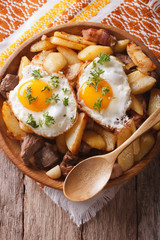 fried potatoes with meat and eggs close-up in a bowl. vertical top view
