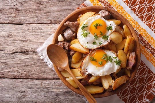 fried potatoes with meat and eggs in a bowl. Horizontal top view
