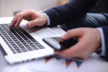 Fototapeta premium Businessman at his workplace uses a smartphone and laptop