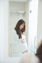 Asian pregnant woman posing in front of a mirror, smiling proudl
