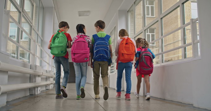 Rear view of school kids with backpacks walking along corridor 