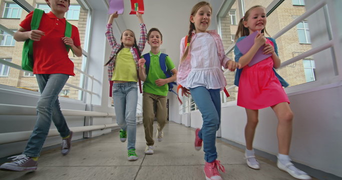 Happy elementary students running along corridor towards the camera 