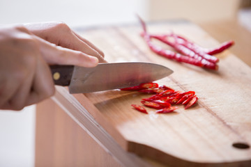 Hand slicing chilli pepper  on wooden background.