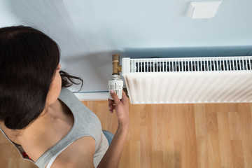 Young Woman Turning Thermostat On Radiator