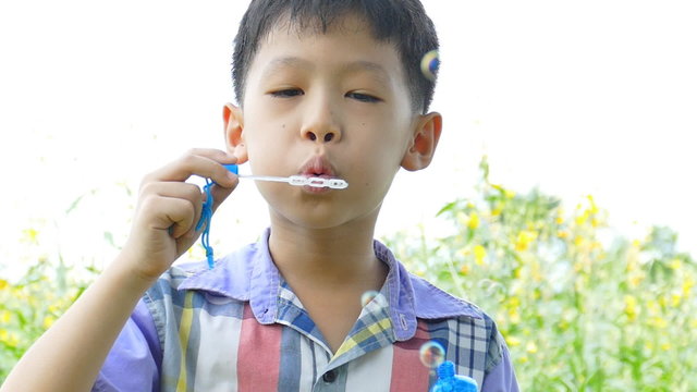 Young Asian boy blowing bubbles in garden 