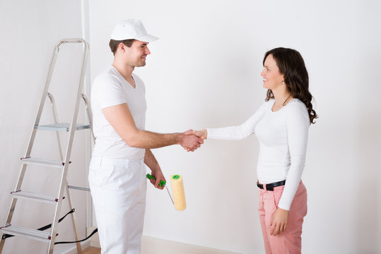 Woman Shaking Hands To Painter With Paint Roller At Home