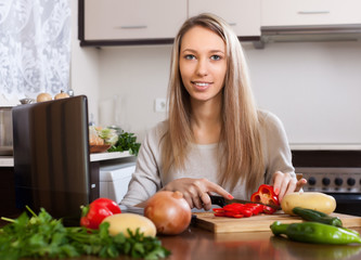 Obraz na płótnie Canvas Blonde woman using notebook during cooking vegetables