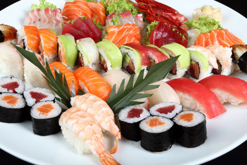 close-up sushi and sashimi mixed on round white plate
