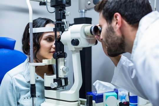  Optician examining womans eyes through slit lamp