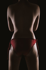 Naklejka premium Portrait of a topless Asian sexy woman in red lingerie showing her smooth skinned back isolated over black background.