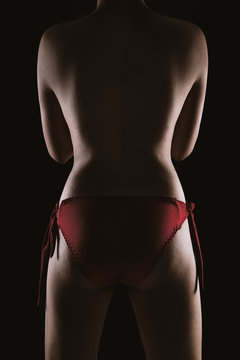 Portrait of a topless Asian sexy woman in red lingerie showing her smooth skinned back isolated over black background.