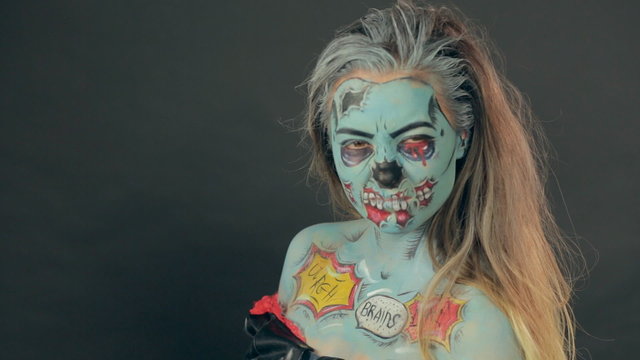 Girl made up as a zombie posing in the studio on a gray
