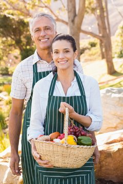  Two mature happy farmers holding a basket of vegetables