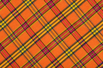 Scottish tartan pattern. Orange and yellow plaid print as background. Symmetric rhombus pattern.