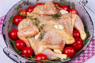 Whole fresh raw chicken prepared for roast with thyme and tomatoes cherry