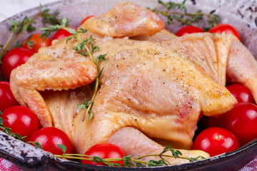 Whole fresh raw chicken prepared for roast with thyme and tomatoes cherry