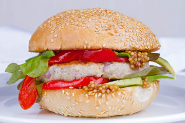 Home cooked burger with turkey, avocado, lettuce, onions, red paprika pepper on a sesame seed bun