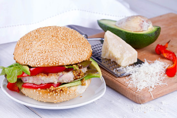 Home cooked burger with turkey, avocado, lettuce, onions, red paprika pepper on a sesame seed bun