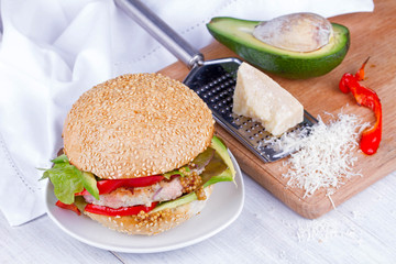 Home cooked burger with turkey, avocado, lettuce, onions, red paprika pepper on a sesame seed bun