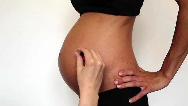 schwangere Frau bekommt ein Herz auf den Bauch gemalt