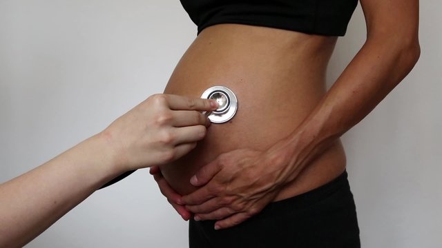 eine schwangere Frau wird am Bauch mit einem Stethoskop abgehört