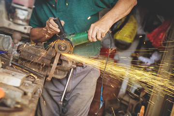 Sparkles. Craftsman sawing metal with disk grinder in workshop.