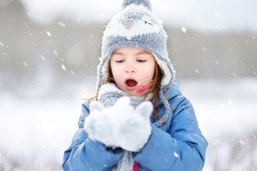 Fototapeta na wymiar Funny little girl catching snowflakes in winter park