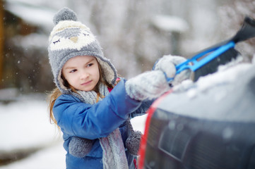 Adorable little girl helping to brush a snow