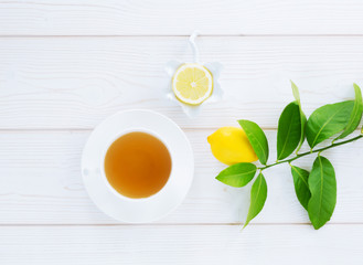 white cup with black tea and lemon yellow on a green branch on a white wooden background