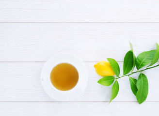 white cup with black tea and lemon yellow on a green branch on a white wooden background